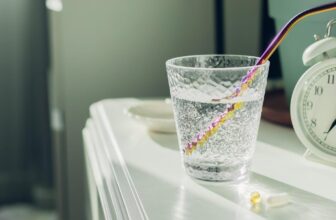 CBD vs melatonin — glass of water and alarm clock on bedside table