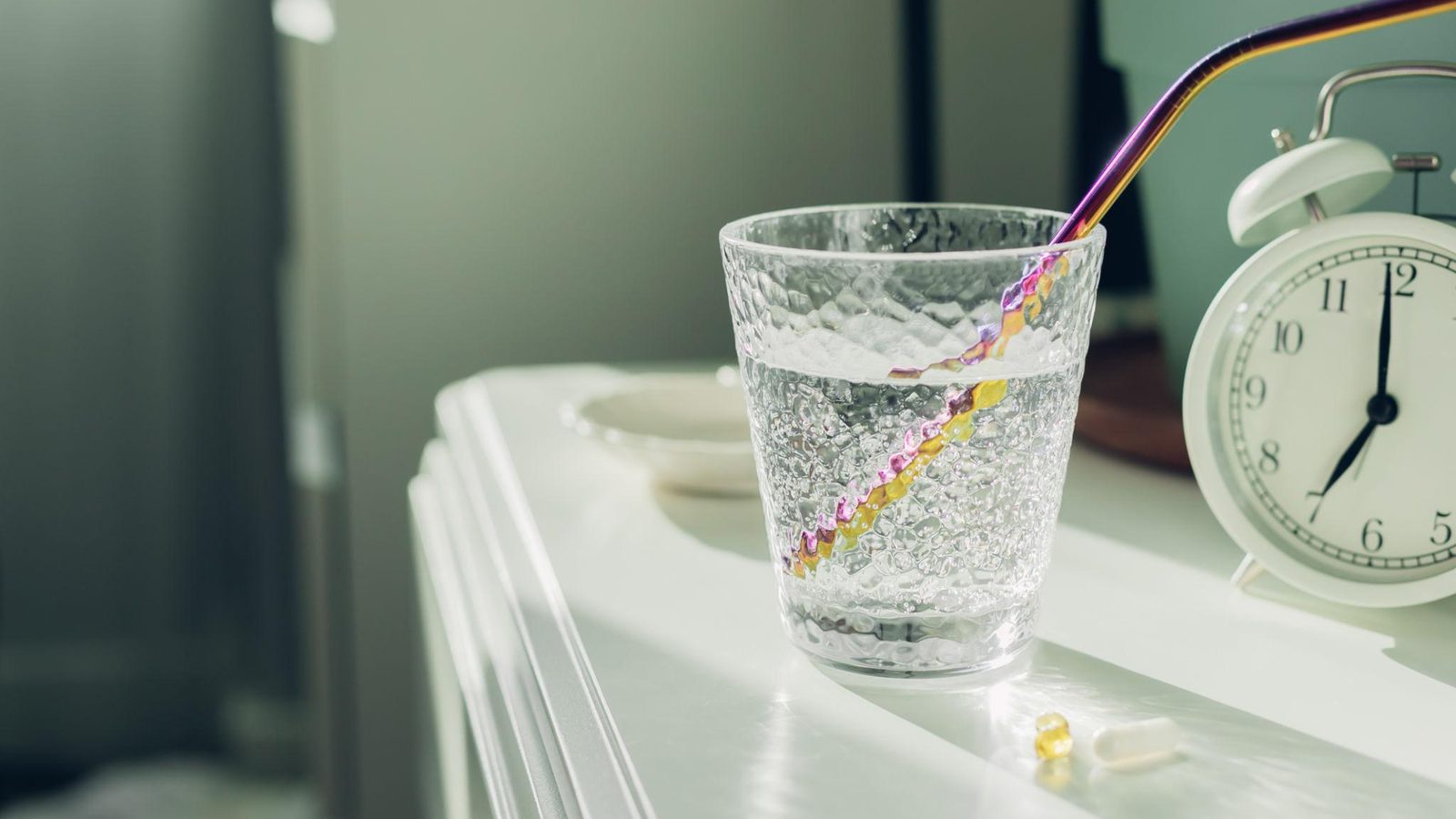 CBD vs melatonin — glass of water and alarm clock on bedside table