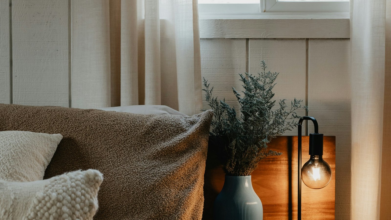 Bedside table with linen pillow, warm lamp, and natural elements in soft evening light