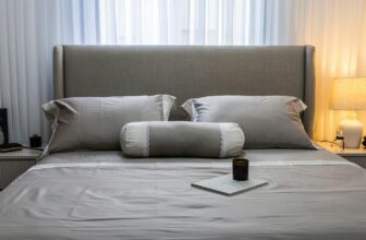 A neatly made bed with soft grey bedding and a warmly lit bedside lamp, set up for a good night's sleep.
