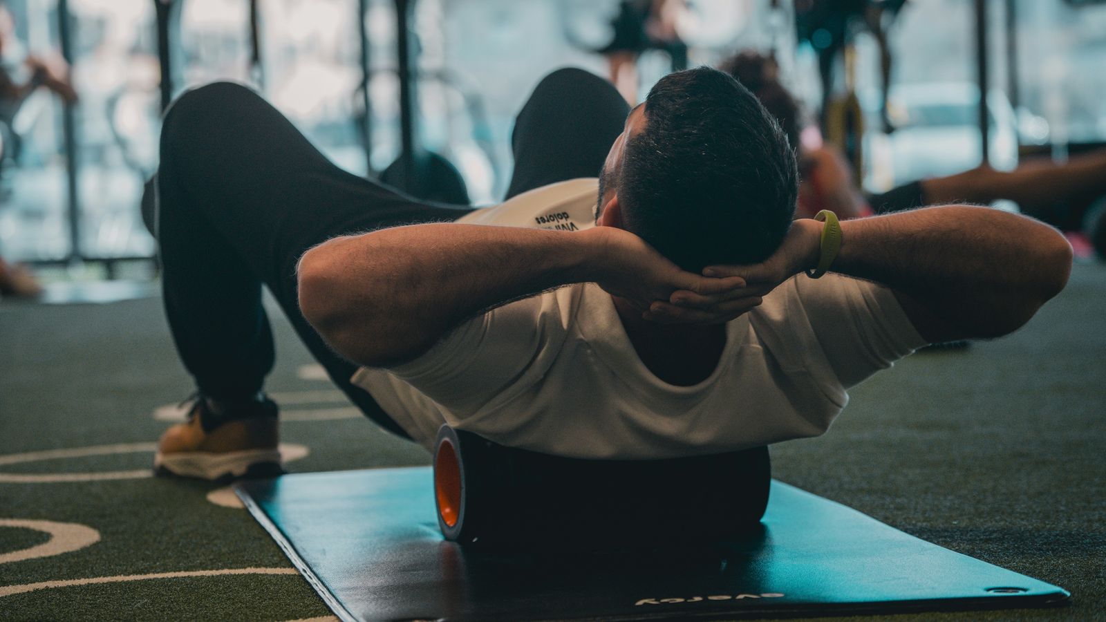 A person lying on a mat foam-rolling their upper back at the gym — active muscle recovery after exercise.