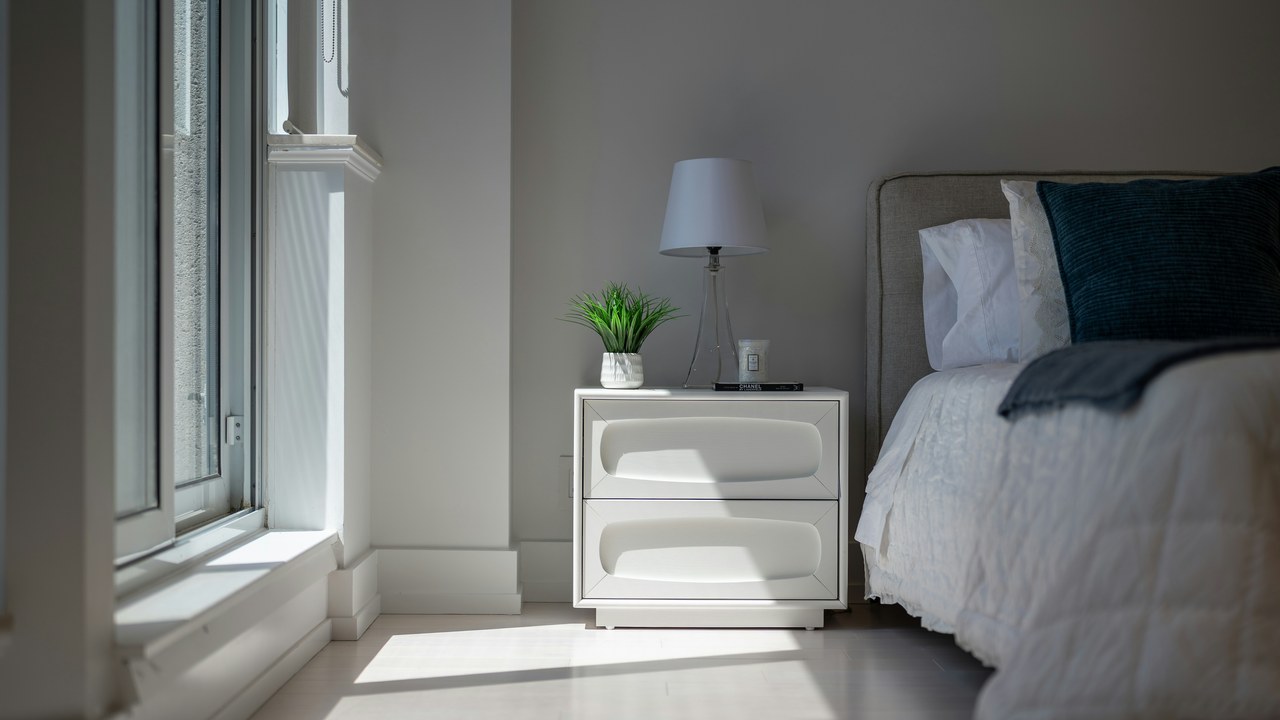 A cool, calm, uncluttered bedroom with light bedding by a window.