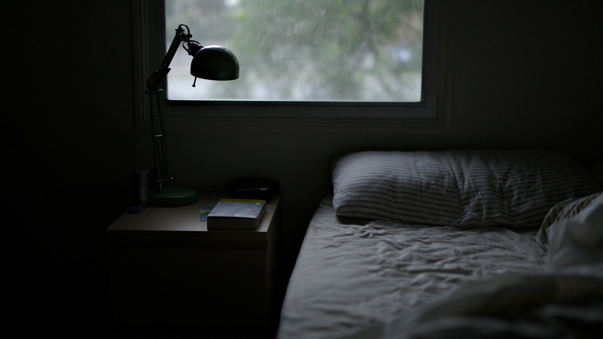 A cool, dim, tidy bedroom with a made bed and soft window light.