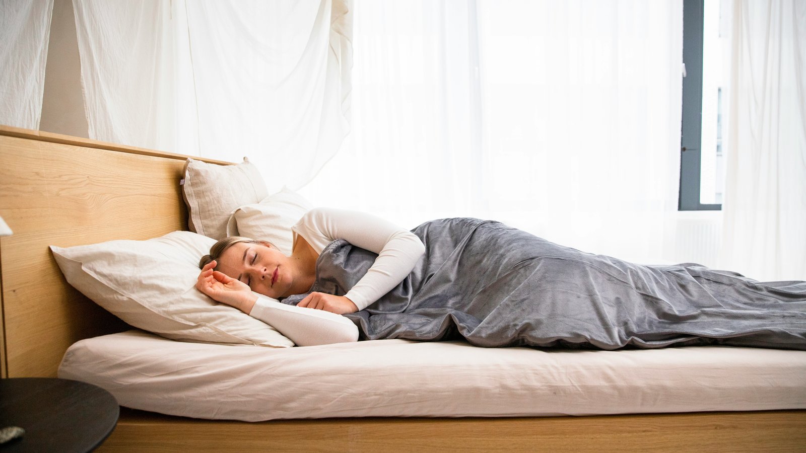 Woman sleeping peacefully on her side in a calm, bright bedroom under a grey blanket