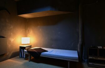 A dark bedroom at night with a single bedside lamp on.