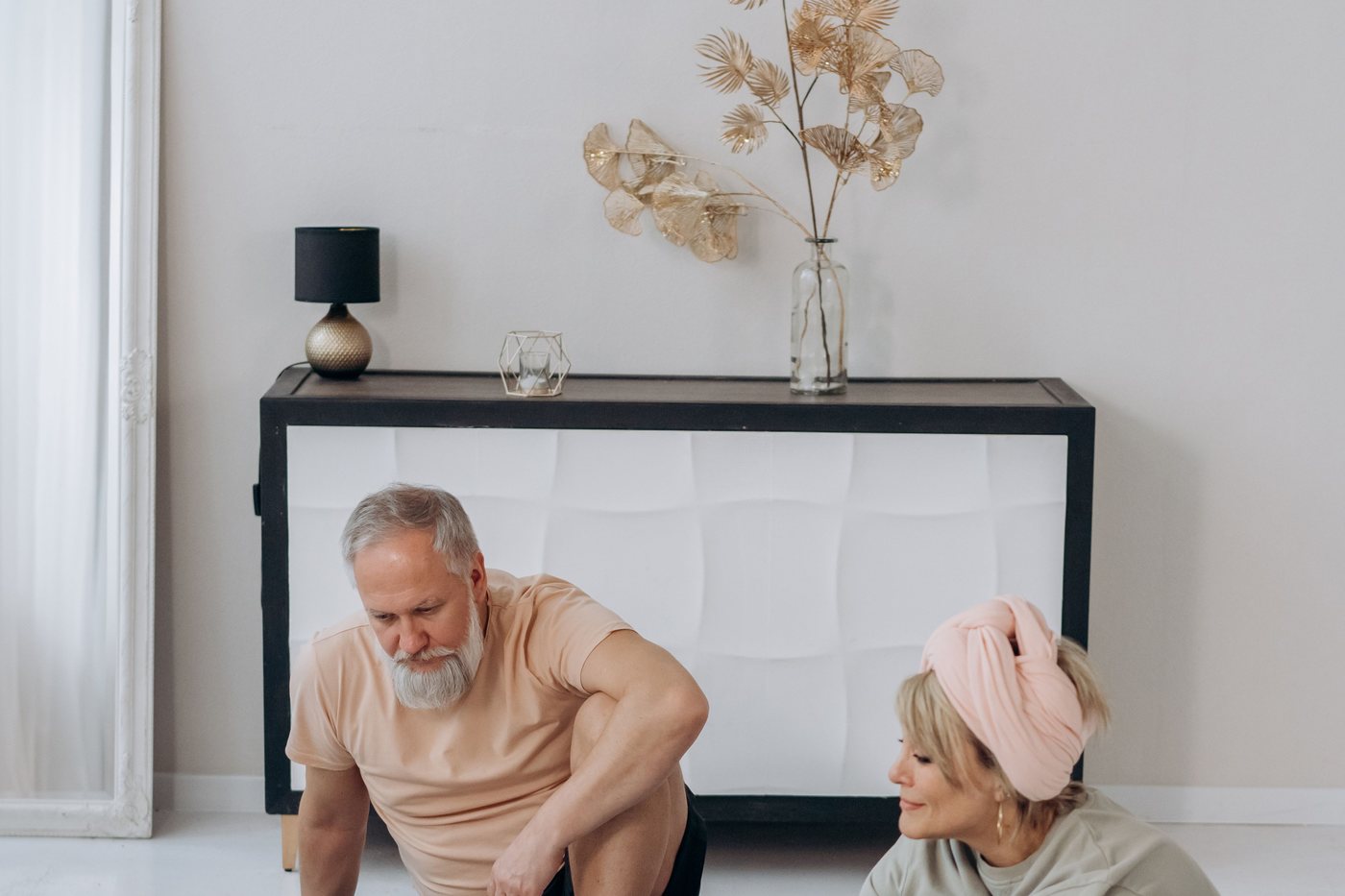 Two older adults stretching on the floor of a living room