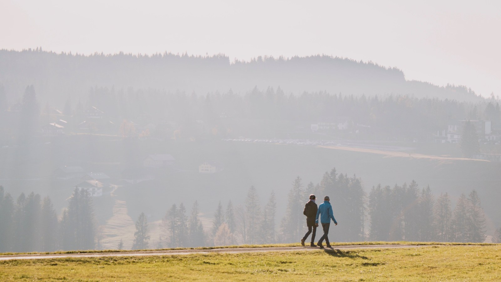 Two people walking a path across a misty hillside at dawn