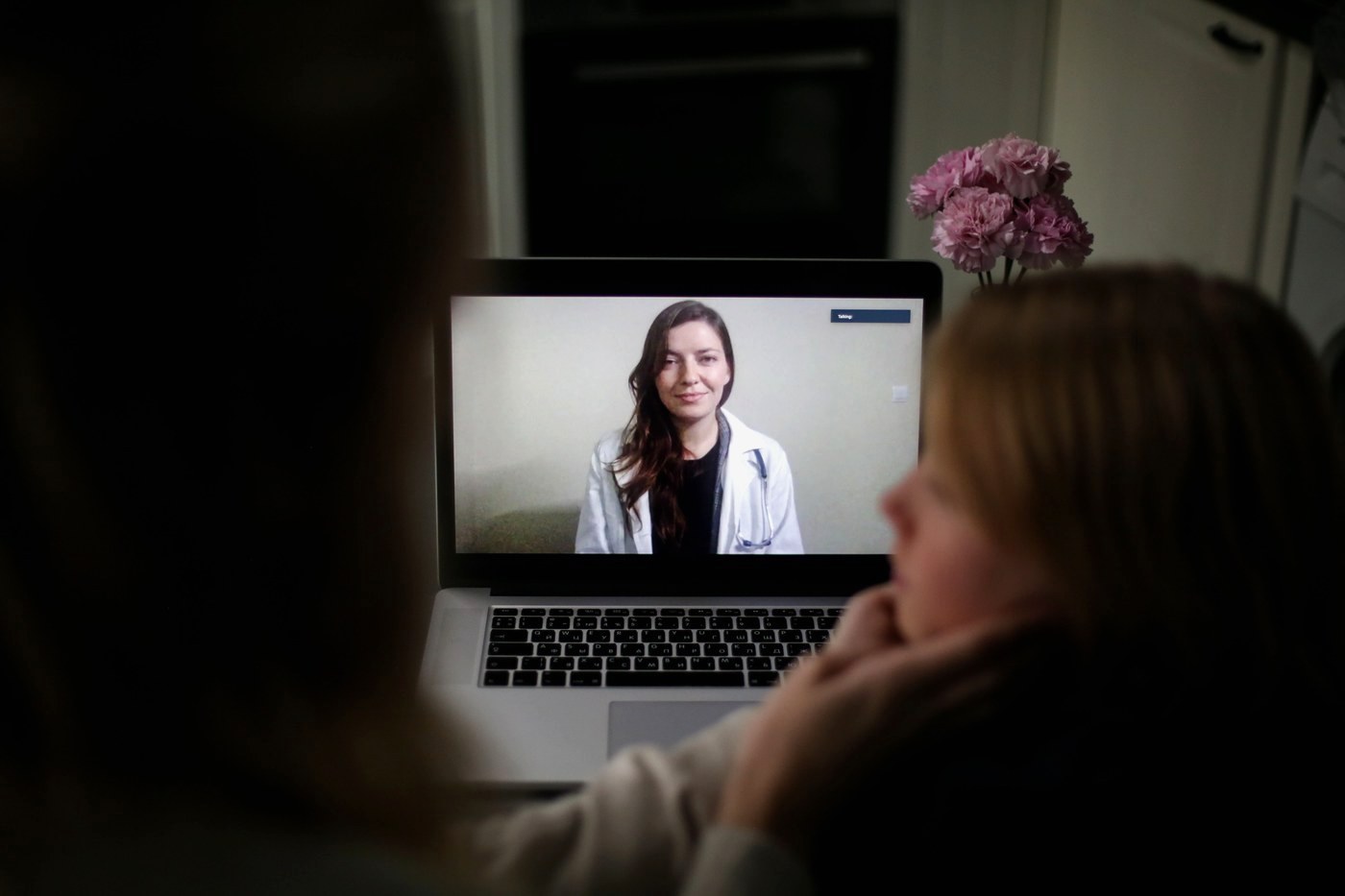 Two people at home speaking with a clinician on a laptop video call