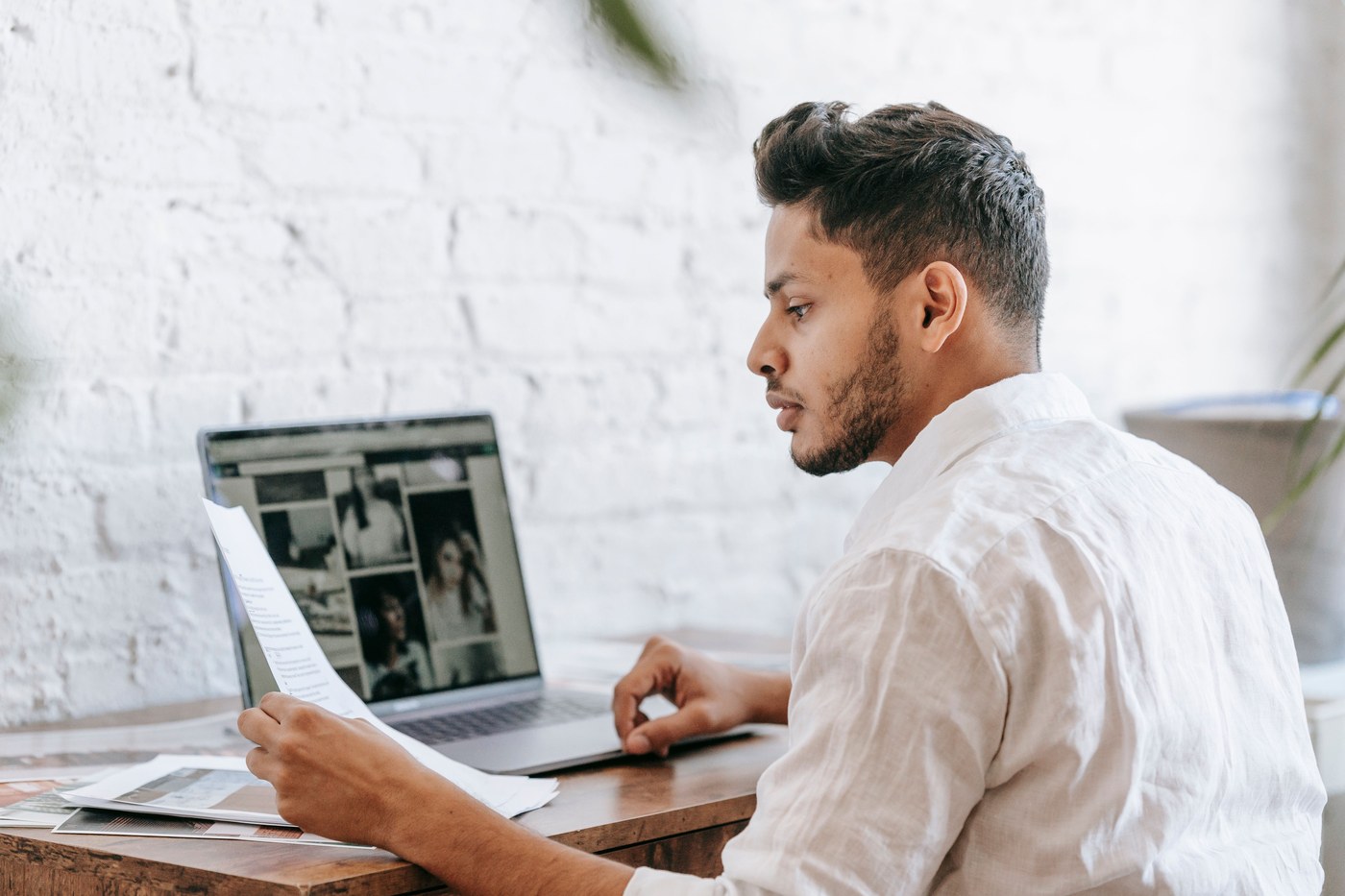 A man reading a printed document beside an open laptop