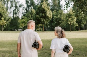 Two older adults carrying exercise mats across a park