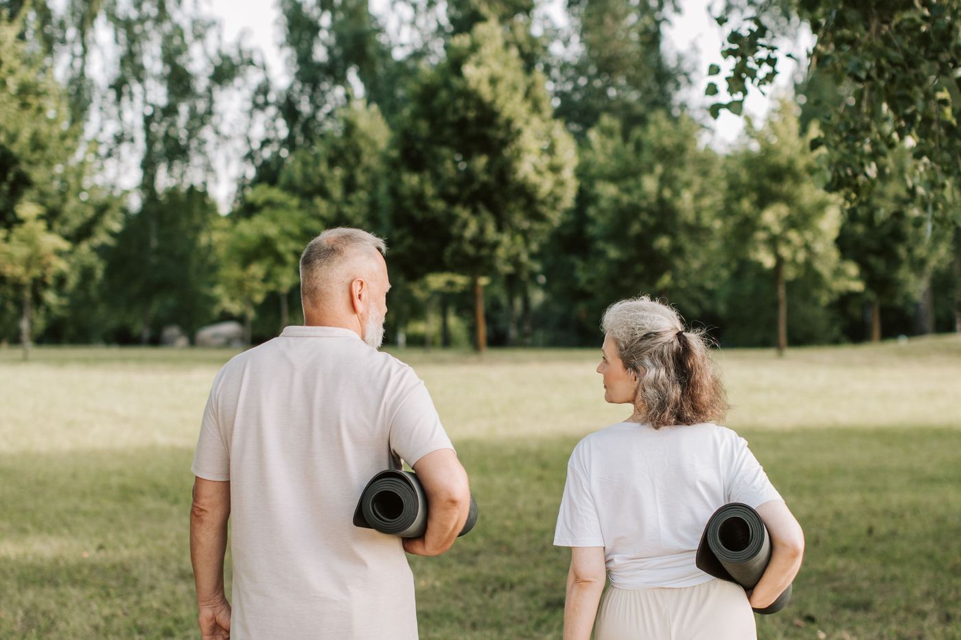 Two older adults carrying exercise mats across a park